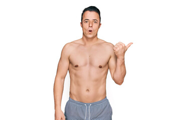 Fototapeta premium Handsome young man wearing swimwear shirtless surprised pointing with hand finger to the side, open mouth amazed expression.