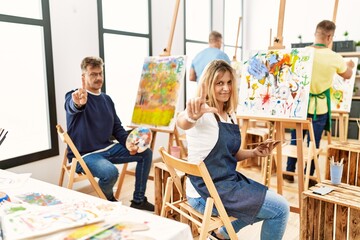 Group of middle age artist at art studio pointing with finger up and angry expression, showing no gesture