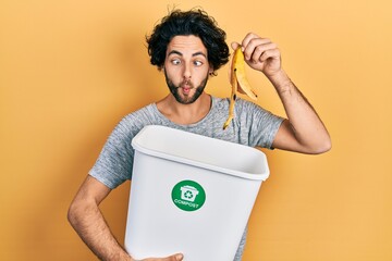 Handsome hispanic man recycling banana peel composting organic fertilizer making fish face with...