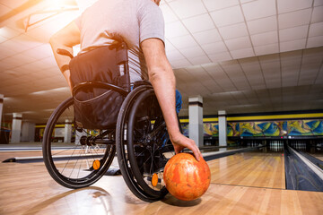 Young disabled man in wheelchair playing bowling in the club