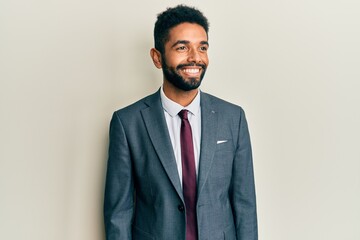 Handsome hispanic man with beard wearing business suit and tie looking away to side with smile on face, natural expression. laughing confident.