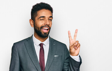 Young african american man wearing business clothes smiling with happy face winking at the camera doing victory sign. number two.