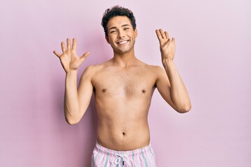 Young handsome man wearing swimwear shirtless showing and pointing up with fingers number nine while smiling confident and happy.