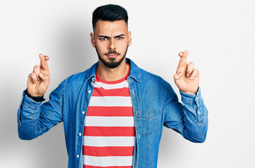 Young hispanic man with beard doing fingers crossed luck gesture skeptic and nervous, frowning...
