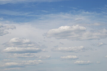 Cumulus and cirrus clouds in the sky. Against the background of a blue sky, various types of clouds, on top of a canvas of high cirrus clouds on the bottom, several cumulus clouds of various sizes.