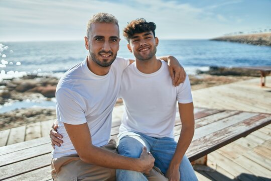Young gay couple smiling happy sitting on the bench at the beach promenade.