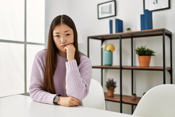 Fototapeta na wymiar Young chinese girl wearing casual clothes sitting on the table at home thinking looking tired and bored with depression problems with crossed arms.