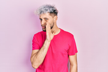 Young hispanic man with modern dyed hair wearing casual pink t shirt hand on mouth telling secret rumor, whispering malicious talk conversation