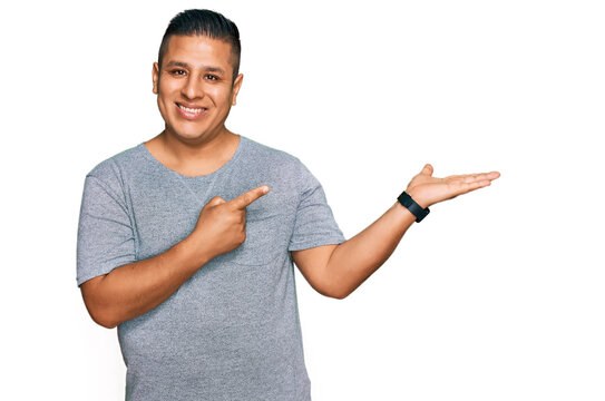 Young latin man wearing casual clothes amazed and smiling to the camera while presenting with hand and pointing with finger.