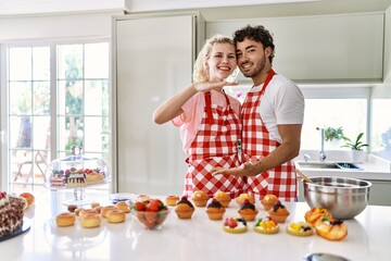 Couple of wife and husband cooking pastries at the kitchen gesturing with hands showing big and large size sign, measure symbol. smiling looking at the camera. measuring concept.