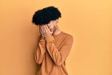 Fototapeta na wymiar Young african american man with afro hair wearing casual winter sweater with sad expression covering face with hands while crying. depression concept.