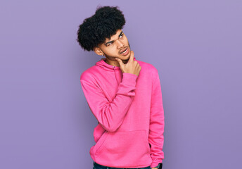 Fototapeta na wymiar Young african american man with afro hair wearing casual pink sweatshirt thinking worried about a question, concerned and nervous with hand on chin