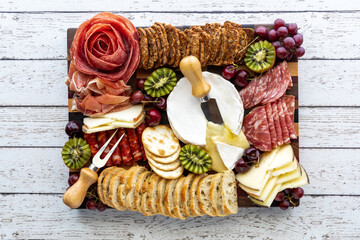Top down view of a meat and cheese charcuterie board on a light wooden table.