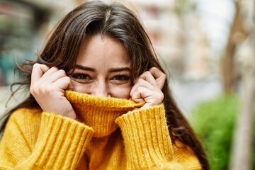 Young beautiful brunette woman wearing turtleneck sweater doing funny gesture covering face with...