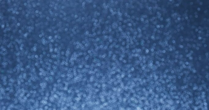 Glittering abstract blue bokeh background. Smoothly increase and decrease the flickering of blue lights. Holiday concept backdrop. Defocused blue particles