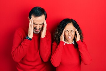 Middle age couple of hispanic woman and man hugging and standing together with hand on head, headache because stress. suffering migraine.