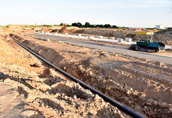 Asphalting the road and laying the sewer pipe at the construction site. Asphalt paver machine...