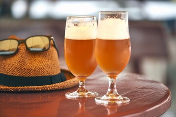 Two glasses of beer on table with straw hat and sunglasses.