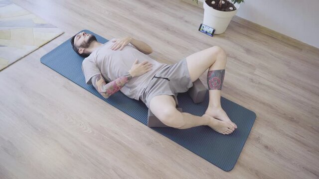 Young man doing Breath awareness exercise lying on yoga mat.