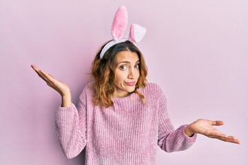 Young caucasian woman wearing cute easter bunny ears clueless and confused with open arms, no idea...