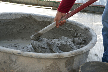 workers use spade mixing wet cement in cement mixing basin, selective focus