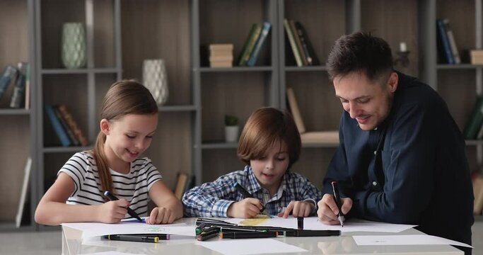 Loving dad and children draw together with color felt pens in album in living room. Happy creative family involved in hobby, create pictures, enjoy communication. Bond, fatherhood, development concept