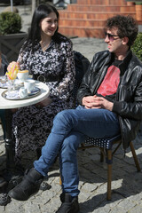 A young married couple is having breakfast in restaurant on terrace. A man and a woman drink coffee and communicate.
