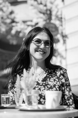 Smiling stylish woman in black shirt with sunglasses sitting at the table drinking coffee in the terrace of restaurant.