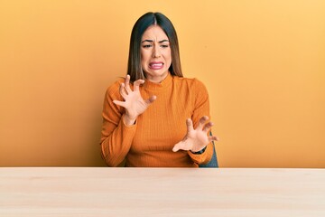 Young hispanic woman wearing casual clothes sitting on the table disgusted expression, displeased...