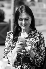 Charming young woman using her smartphone while having cup of coffee. Breakfast on a summer day on terrace in restaurant.