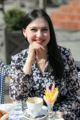 Smiling stylish woman in black shirt sitting at the table drinking coffee in the terrace of restaurant.