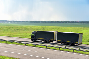 Rigid Truck and Drawbar Trailer driving along highway on the green agriculture field background....