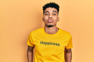 Young african american man wearing t shirt with happiness word message looking at the camera blowing a kiss on air being lovely and sexy. love expression.