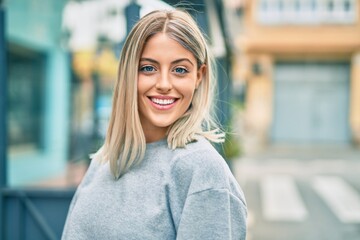 Young blonde girl smiling happy standing at the city.