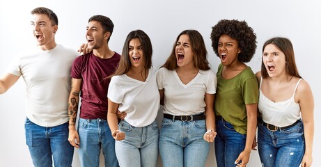 Obraz premium Group of young friends standing together over isolated background angry and mad screaming frustrated and furious, shouting with anger. rage and aggressive concept.