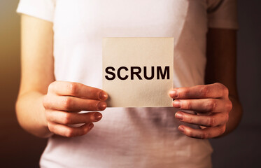 Scrum word on paper in female hand closeup. Concept of methods in management.
