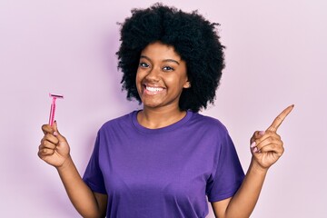 Young african american woman holding razor smiling happy pointing with hand and finger to the side