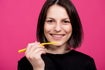 Beautiful happy young woman with single tufted toothbrush on blank pink background