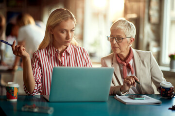 Two female colleagues are watching laptop content while working in the office together
