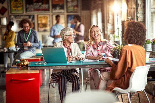 Elderly female boss and her young female colleagues are chatting while enjoying a break at office. Employees, office, work