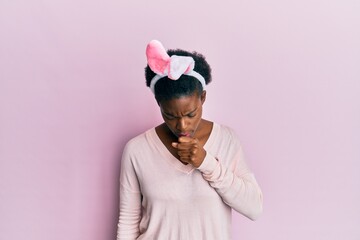 Young african american girl wearing cute easter bunny ears feeling unwell and coughing as symptom...