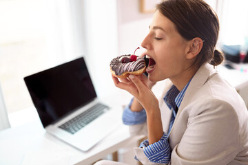 Young businesswoman eating appetizing donuts