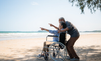 Side view of asian senior couple relaxing smile and enjoying with pointing and look to sea on beach under tree.