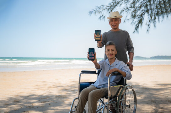 Asian senior couple tourist showing display digital vaccination passport certificate from smartphone at beach.