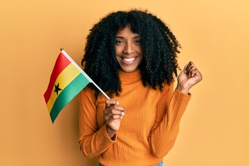 African american woman with afro hair holding ghana flag screaming proud, celebrating victory and success very excited with raised arm