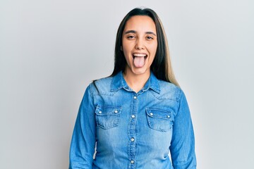 Young hispanic woman wearing casual denim jacket sticking tongue out happy with funny expression. emotion concept.