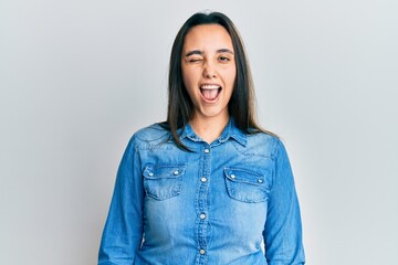 Young hispanic woman wearing casual denim jacket winking looking at the camera with sexy...