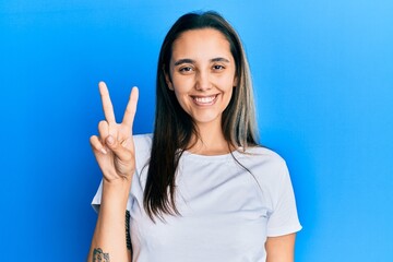 Young hispanic woman wearing casual white t shirt showing and pointing up with fingers number two while smiling confident and happy.