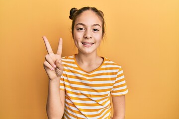 Beautiful brunette little girl wearing casual striped t shirt smiling looking to the camera showing fingers doing victory sign. number two.