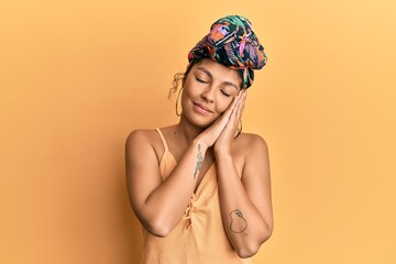Young hispanic girl wearing hair turban over yellow background sleeping tired dreaming and posing...